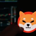 Das Logo der Memecoin Shiba Inu (SHIB) auf einem Handy mit dem Kurs im Candlestick-Chart im Hintergrund, auf einer Kryptobörse