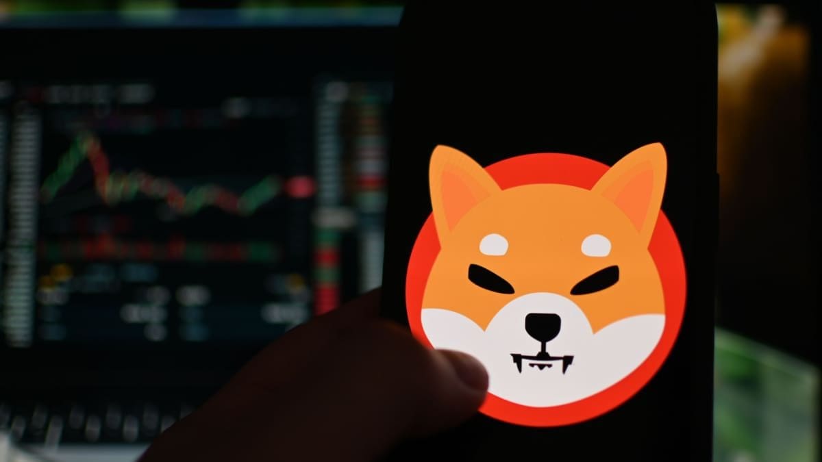 Das Logo der Memecoin Shiba Inu (SHIB) auf einem Handy mit dem Kurs im Candlestick-Chart im Hintergrund, auf einer Kryptobörse
