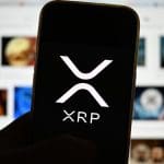Ein Bild des XRP-Logos auf einem Mobiltelefon mit Medien im Hintergrund, die sich auf Ripple und deren Währung XRP beziehen.