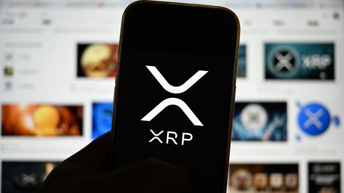 Ein Bild des XRP-Logos auf einem Mobiltelefon mit Medien im Hintergrund, die sich auf Ripple und deren Währung XRP beziehen.
